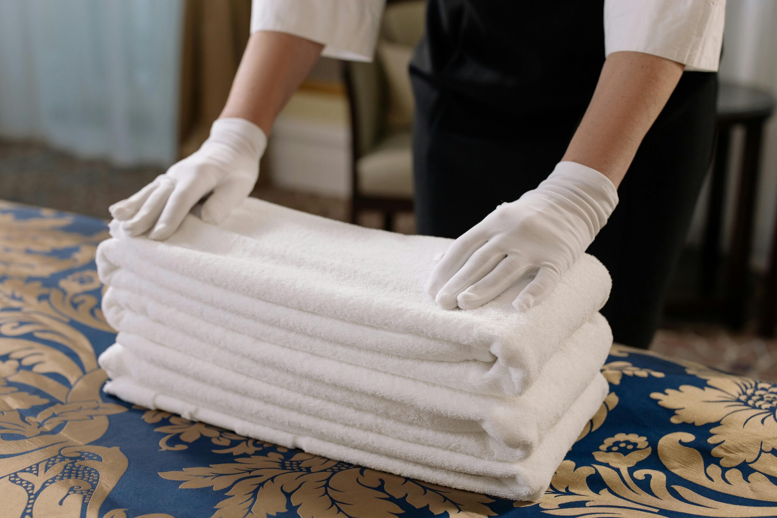 Professional housekeeper folding clean towels on a bed in a hotel room, emphasizing neatness and service.