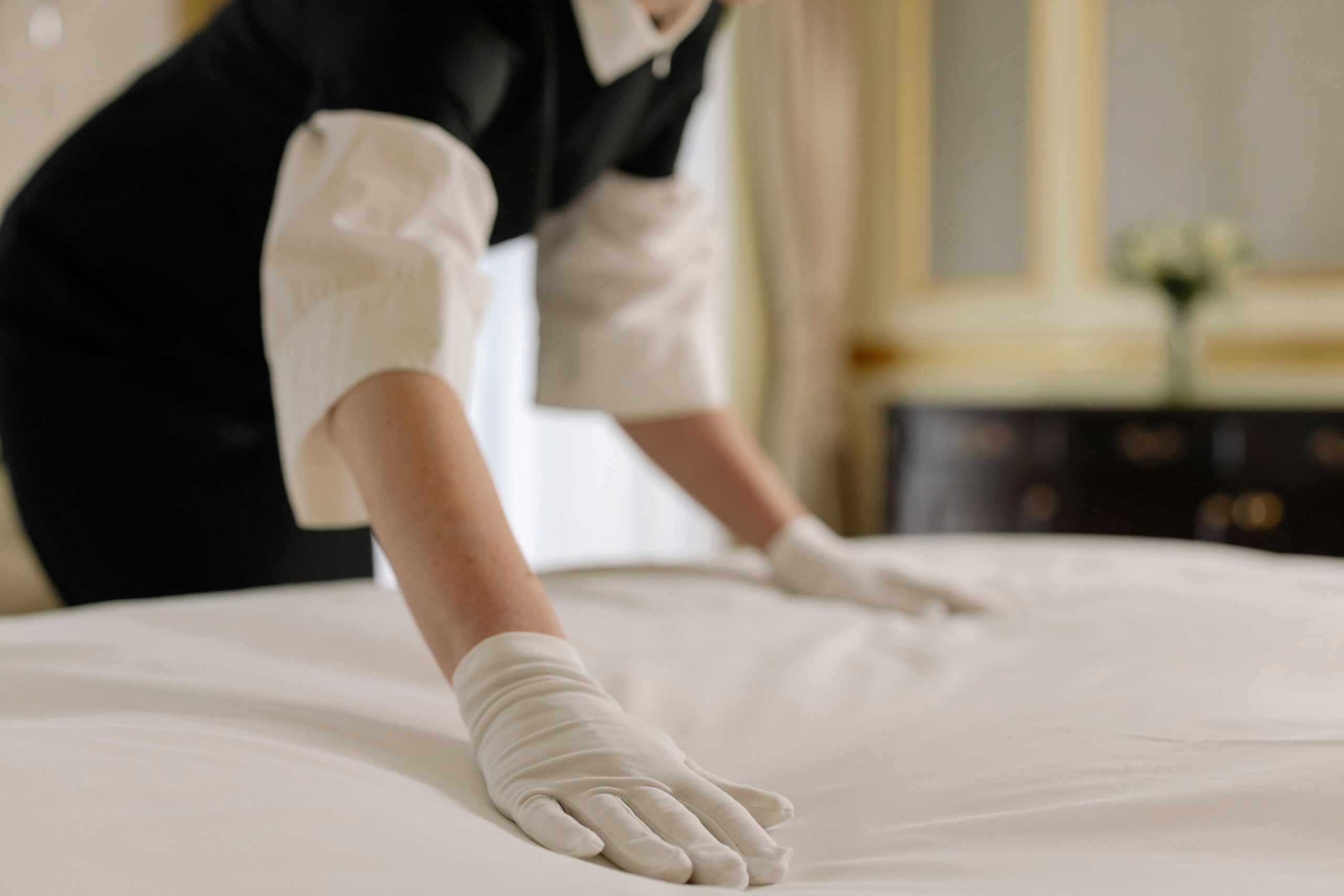 A housekeeper straightening the bed linens in a well-appointed hotel room.